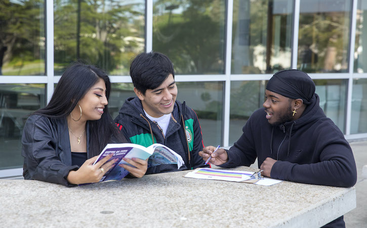 Three students outside studying and talking